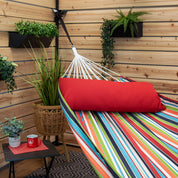 A colourful striped hammock with a red pillow suspended in a backyard patio