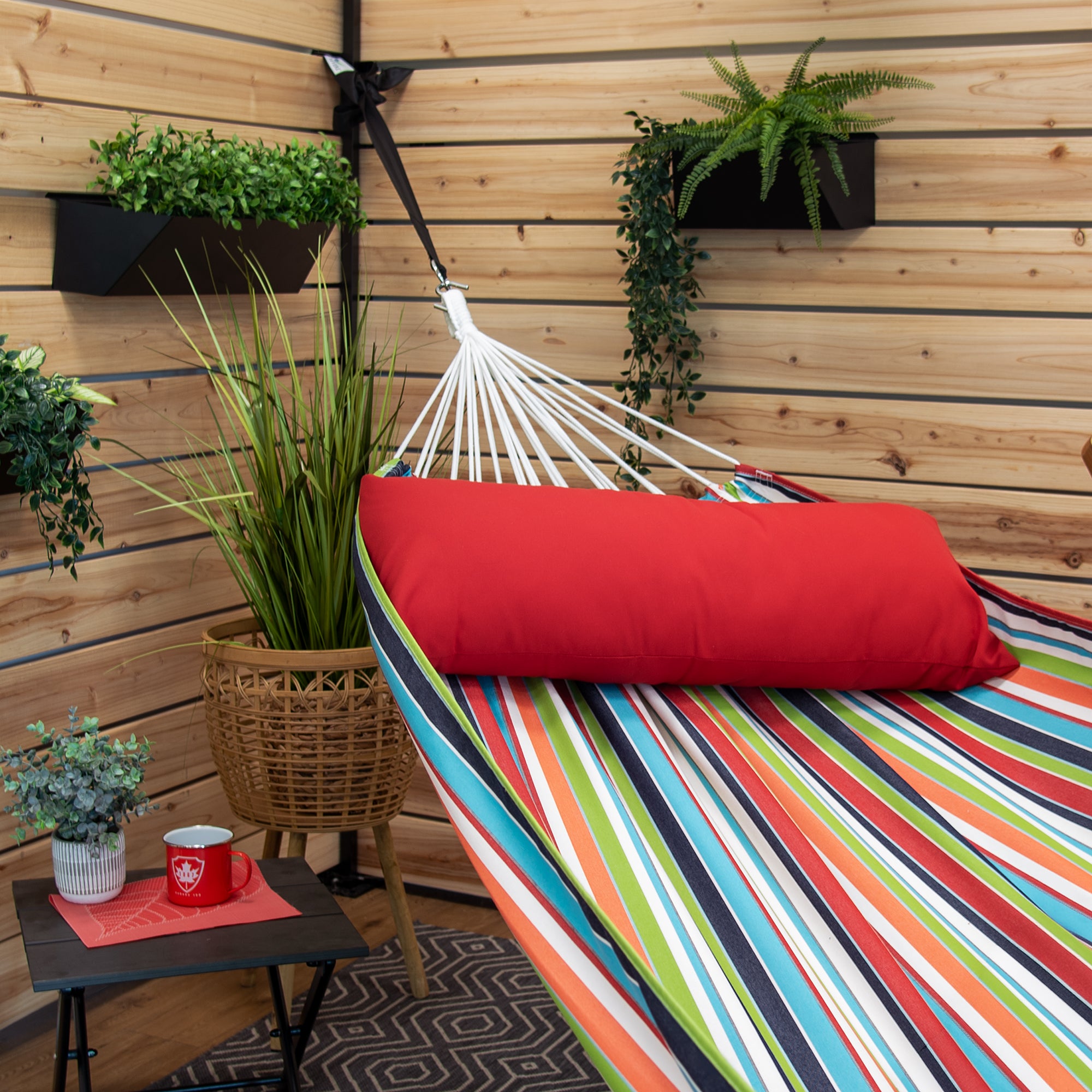 A colourful striped hammock with a red pillow suspended in a backyard patio
