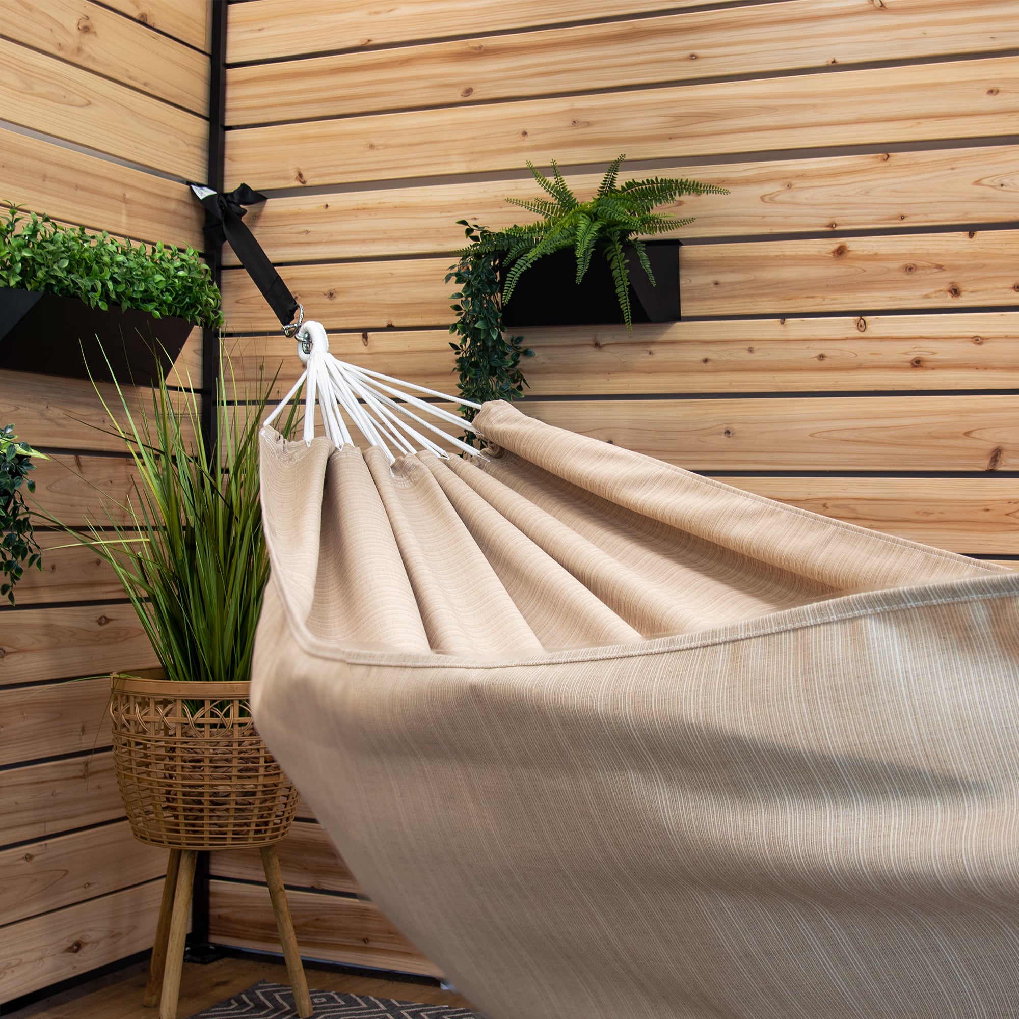 A Sunbrella hammock in sand suspended in a backyard patio